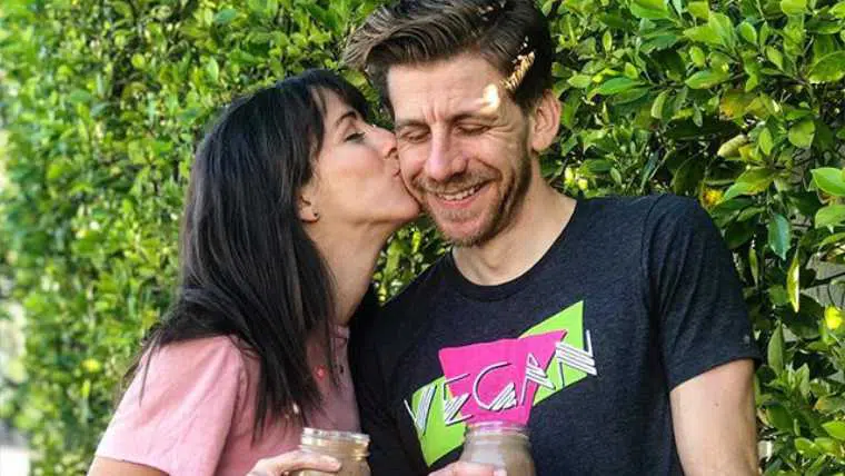 Ana and Brian from Those Annoing Vegans standing in front of some greenery holding a glass of smoothie each