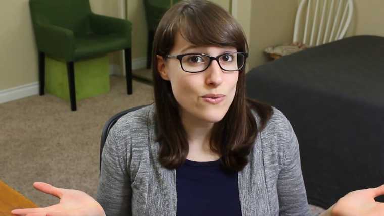 Swayze from Unnatural Vegan sitting in her living room, wearing a grey sweater and black glasses