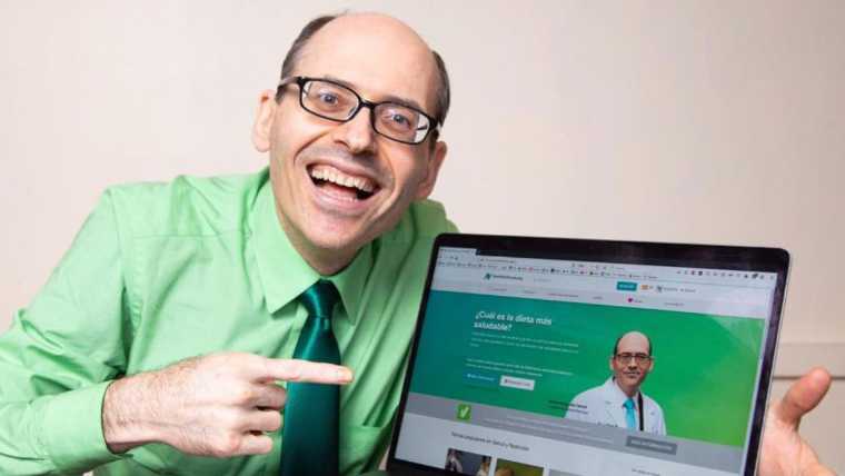 Dr. Greger from Nutritionfacts smiling and pointing at laptop screen that shows nutritionfacts website
