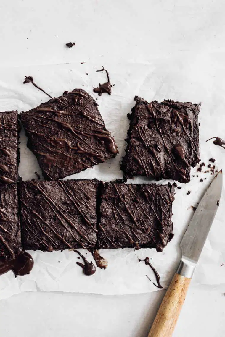 white parchment paper with six black bean brownie squares next to a knife