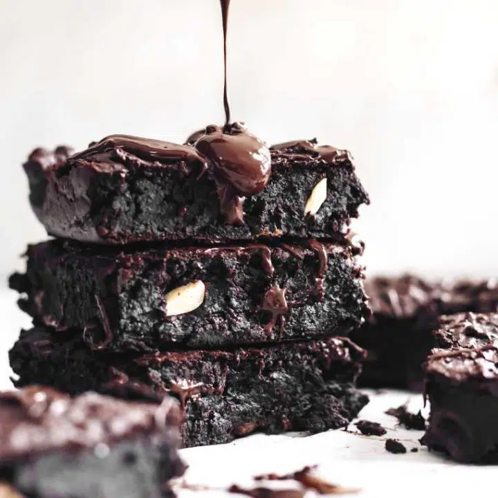 three homemade black bean brownies on top of each other being drizzled with melted chocolate