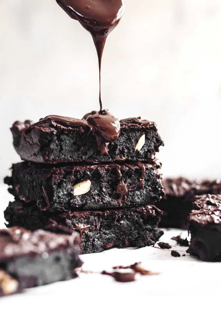 three homemade black bean brownies on top of each other being drizzled with melted chocolate