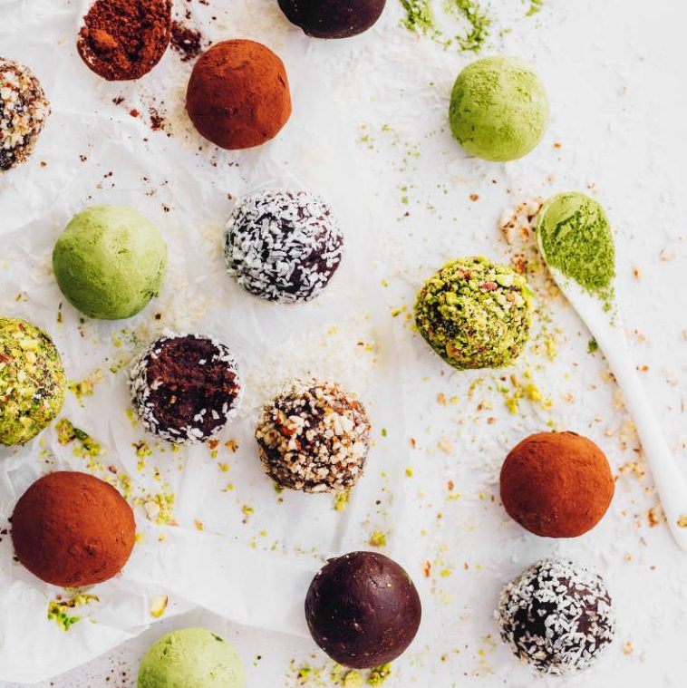white parchment paper with different colored bliss balls covered with coconut, matcha, cocoa and different nuts