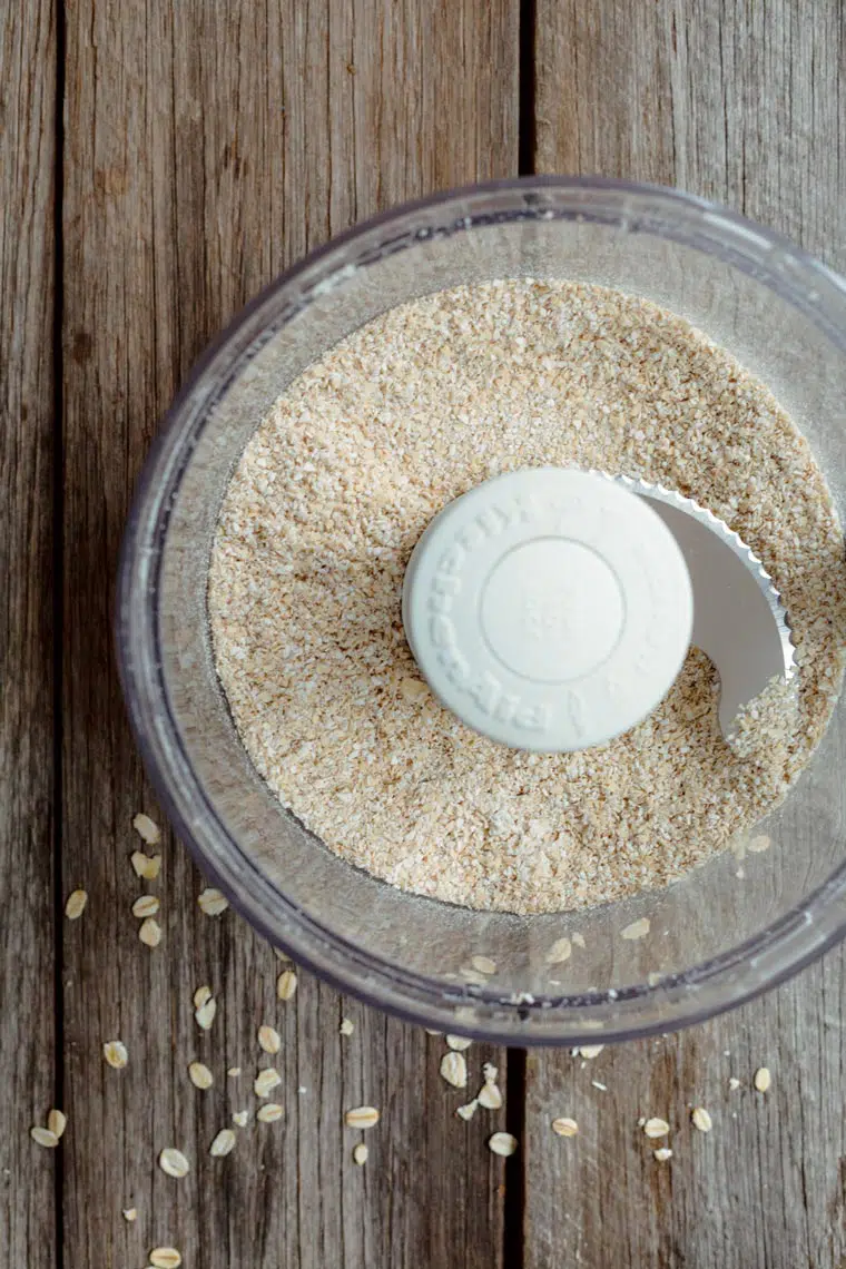 top view of a food processor on a wooden table with finely ground oats inside