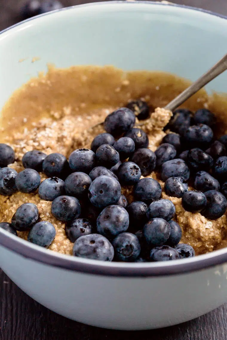 white bowl with mixed gluten-free batter for muffins topped with fresh blueberries