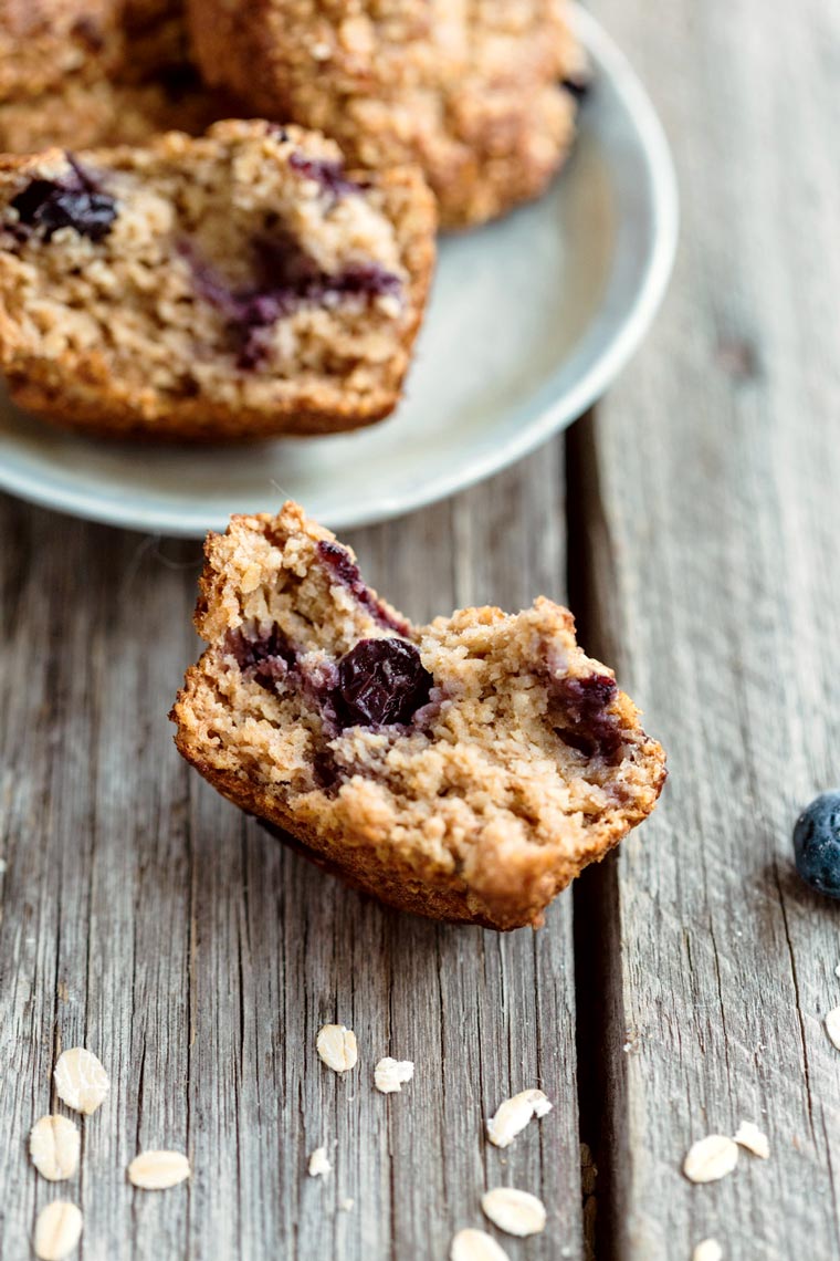 close-up on a half-eaten gluten-free vegan blueberry muffin showing its fluffy texture next to a plate with more muffins