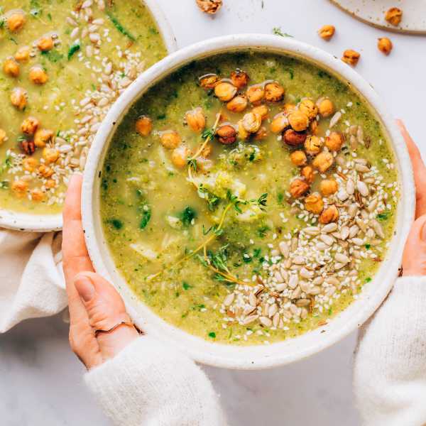 Hands holding green soup with chickpea topping