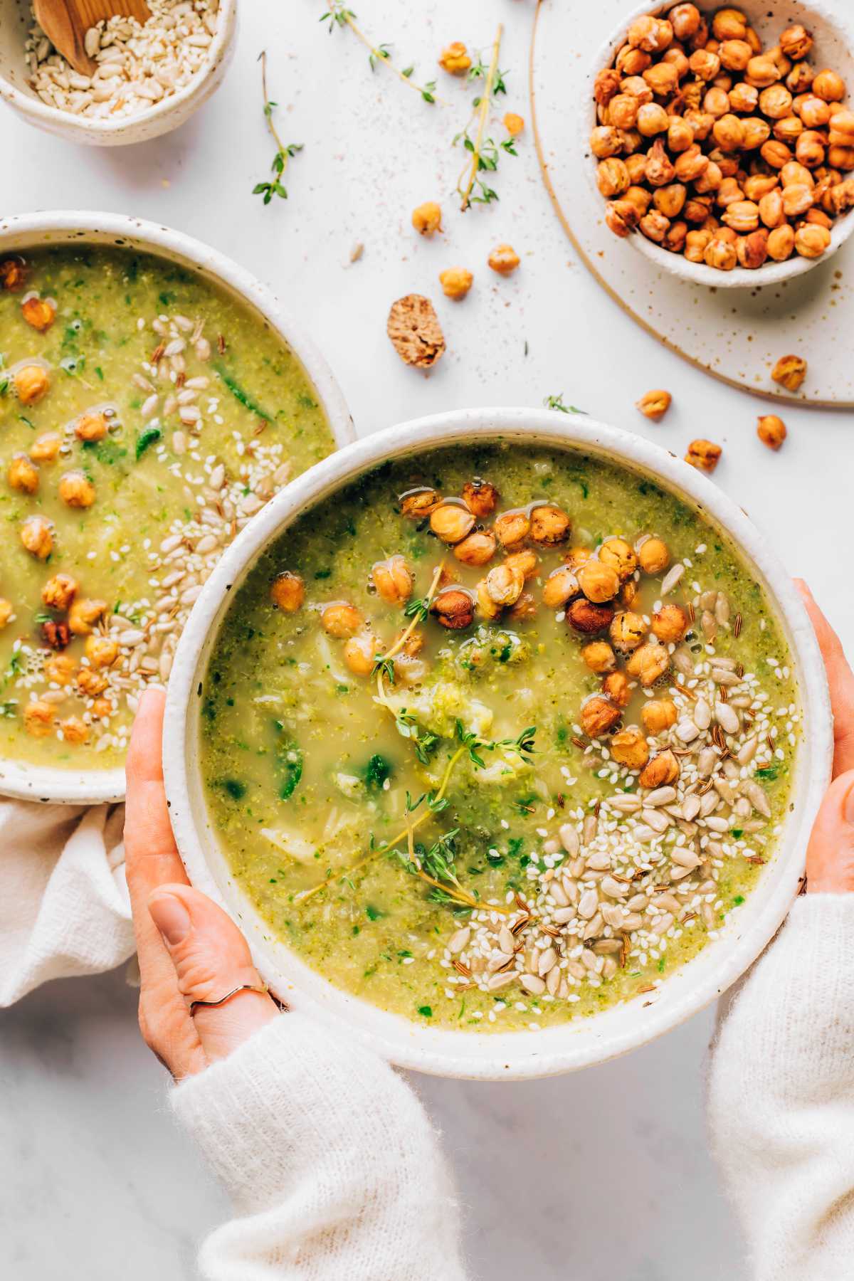 two hands holding a bowl of vegan broccoli soup with chickpeas