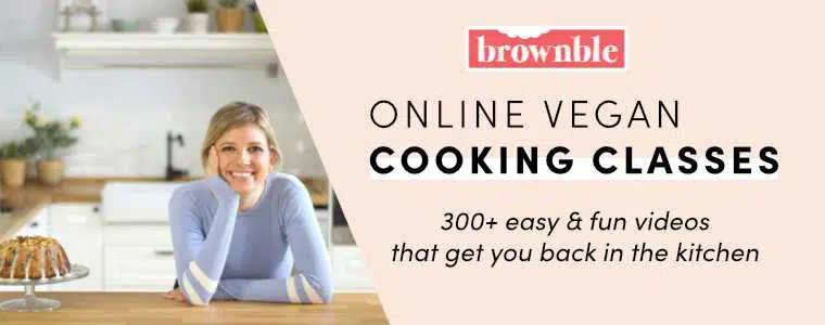 smiling blonde woman leaning on the wooden counter in her kitchen next to a cake with the words online vegan cooking classes and brownble on the right side
