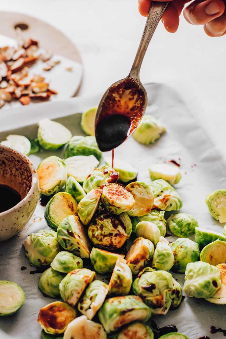 Brussels sprouts on a baking sheet being drizzled with a flavorful sauce