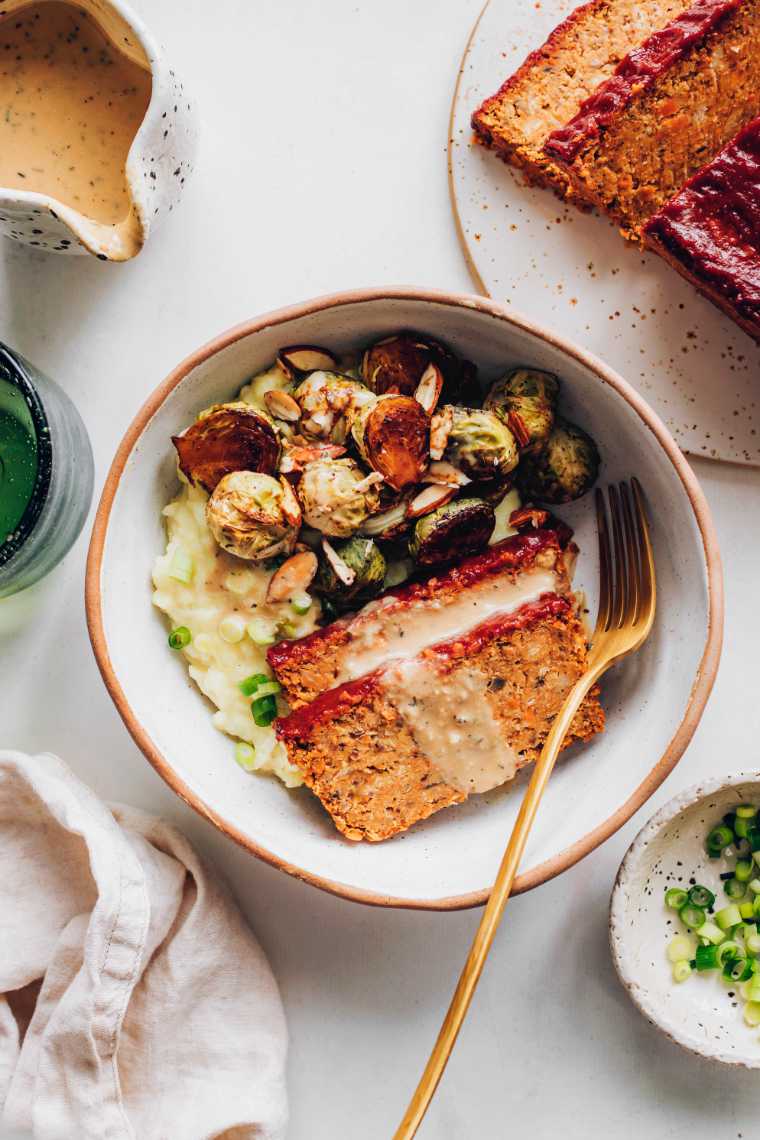 large white bowl with vegan thanksgiving dinner sides like mashed potatoes, brussels sprouts, gravy and chickpea loaf
