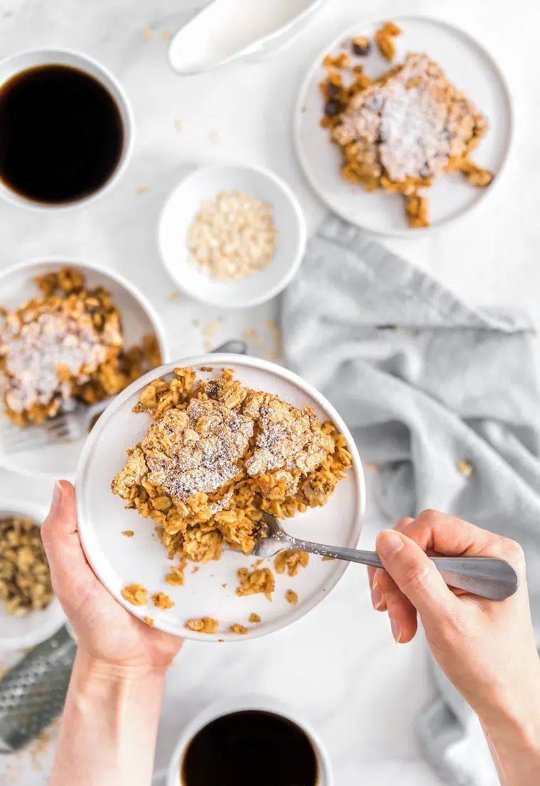 woman holding white plate with a vegan carrot cake oatmeal Christmas breakfast bake over a table of more food