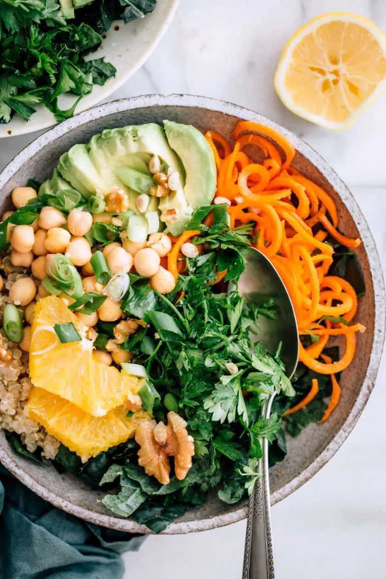 marble table with a bowl of spiralized carrots, quinoa, chickpeas, chopped greens and avocado