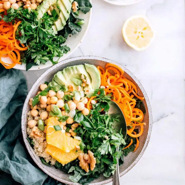 marble table with two bowls of spiralized carrots, quinoa, chickpeas, chopped greens and avocado