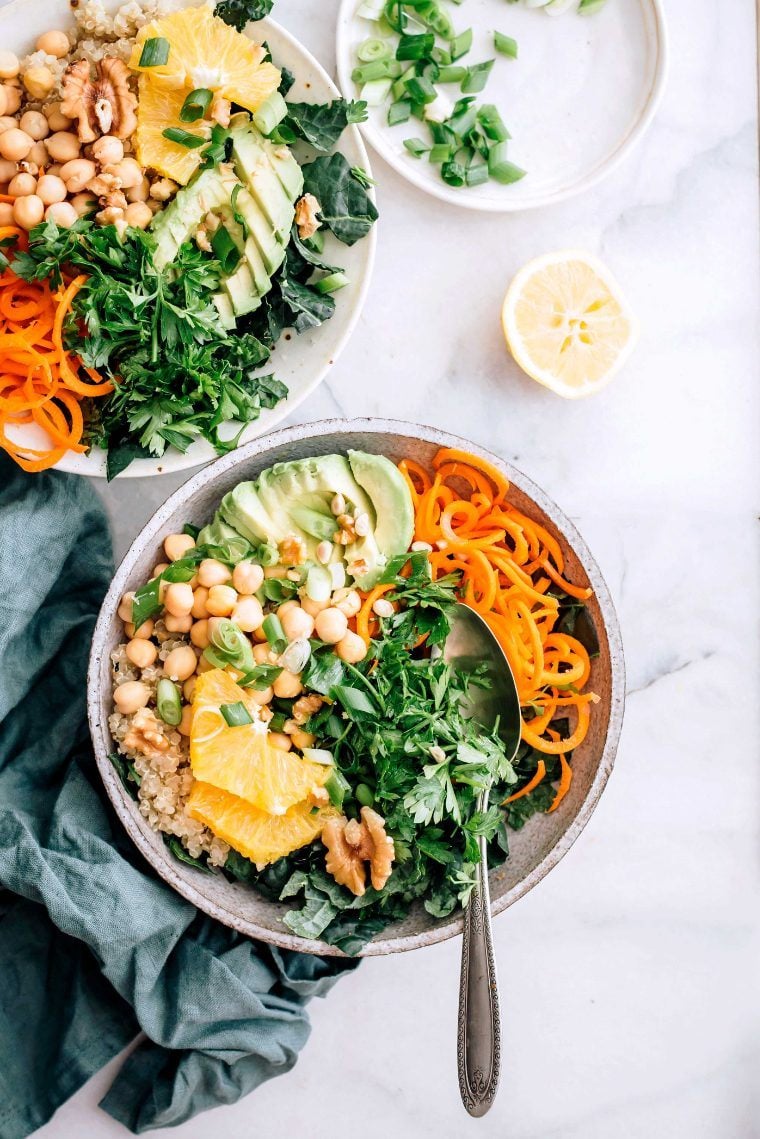 marble table with two bowls of spiralized carrots, quinoa, chickpeas, chopped greens and avocado