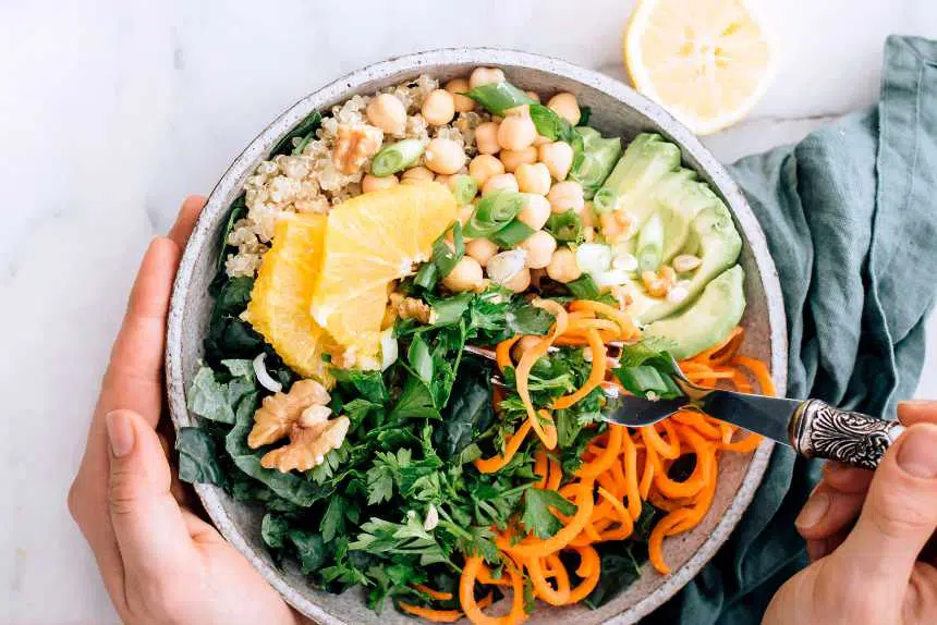 bowl of spiralized carrots, quinoa, chickpeas, chopped greens and avocado with two hands and a spoon