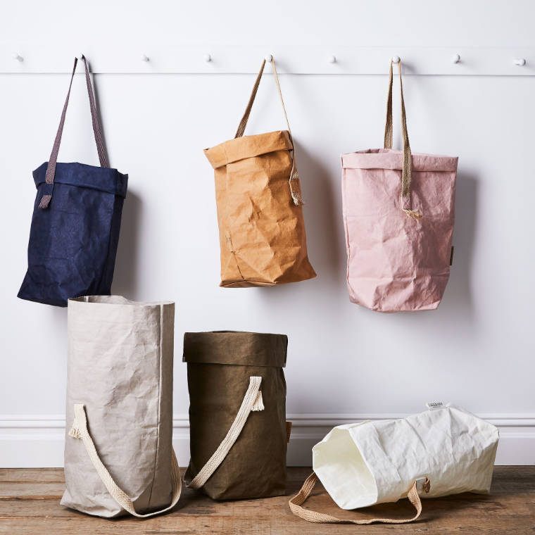 white wall with hangers on which three different colored carry one bags are hanging that are made out of robust paper