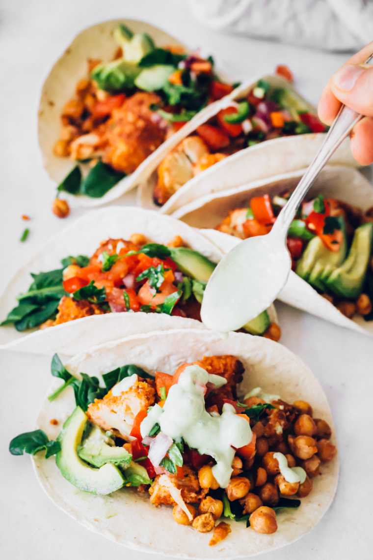five homemade buffalo cauliflower tacos being drizzled with vegan ranch
