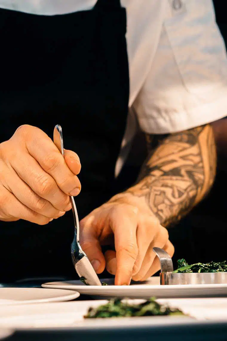 Closeup of male chef with tattoos arranging green vegetables on a plate