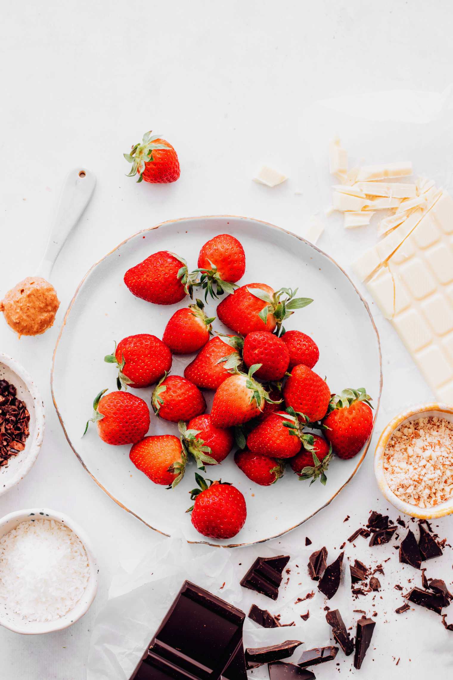 white table with vegan chocolate, fresh strawberries, almond butter and crushed nuts