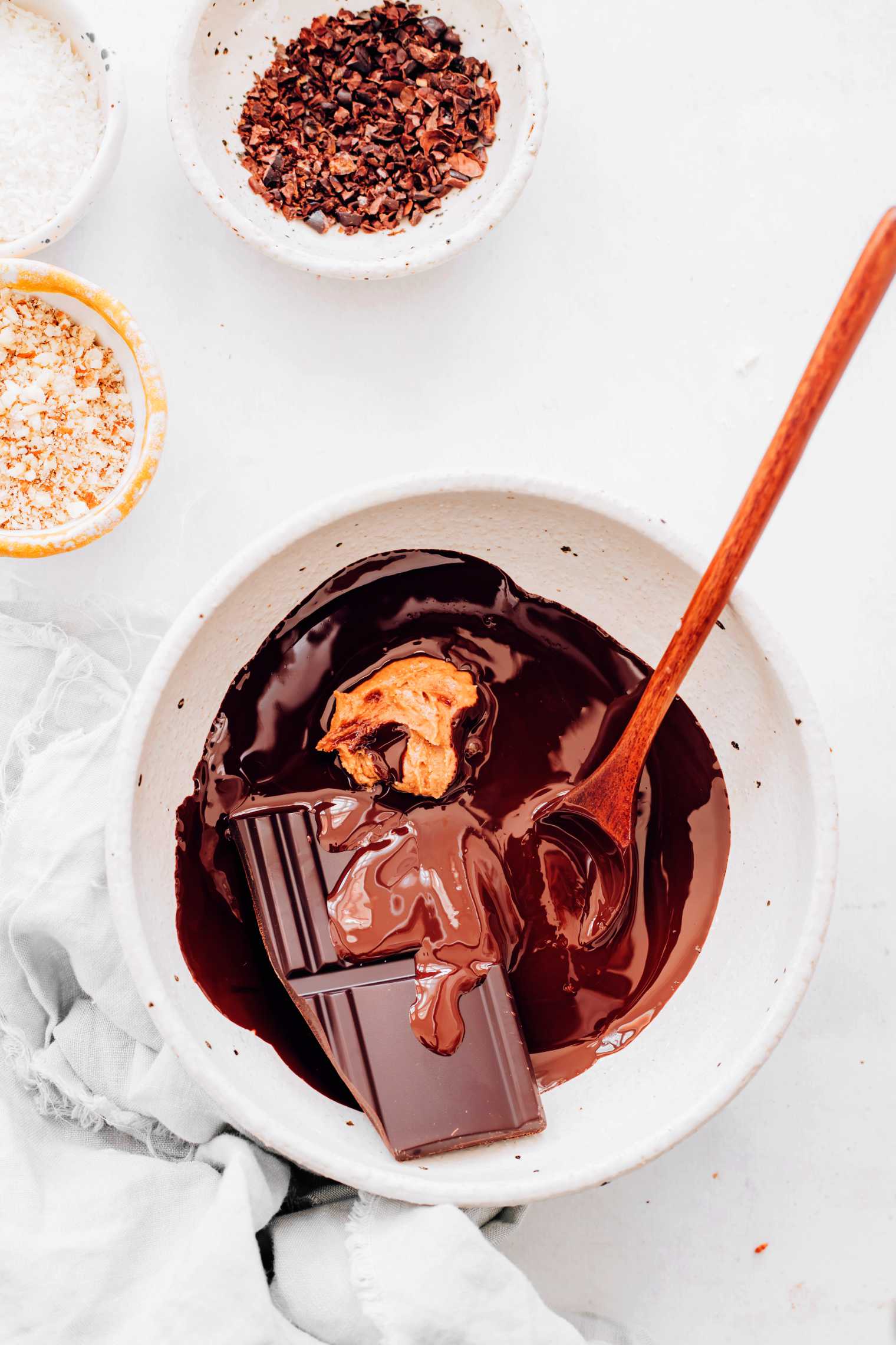 small white bowl on a table with melted chocolate, almond butter and a spoon