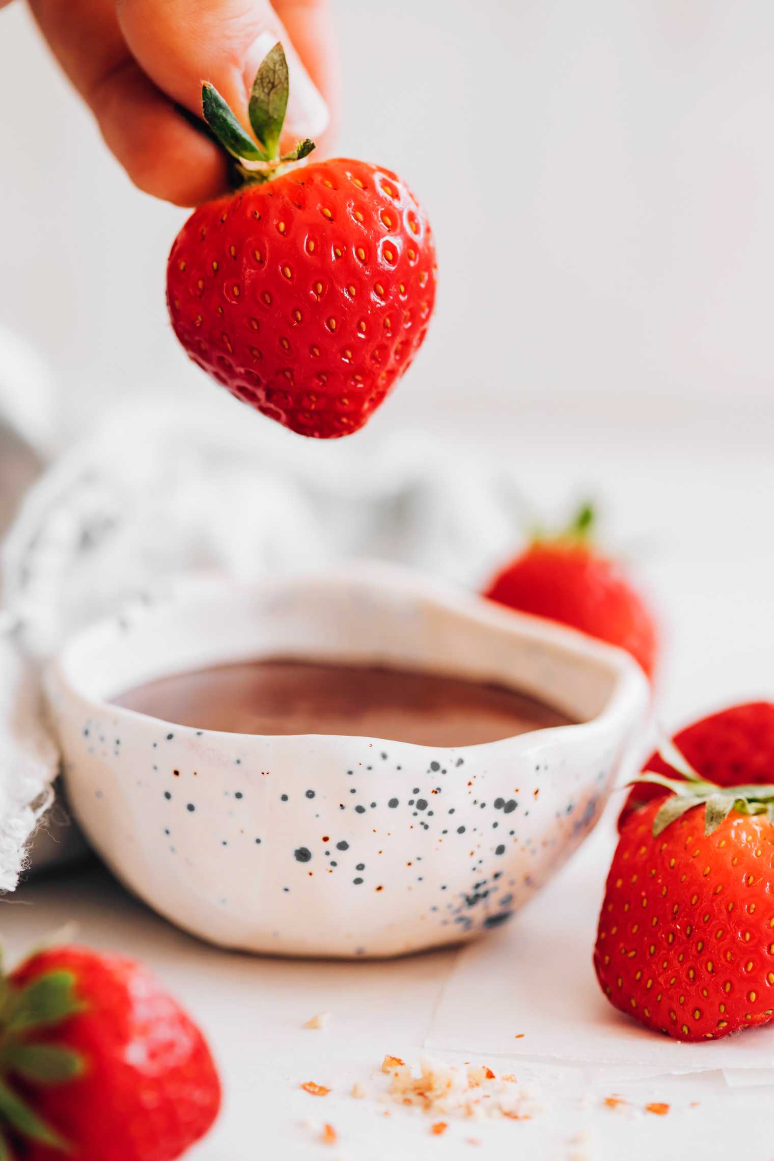 hand holding a strawberry by its leaves over a small bowl of melted chocolate