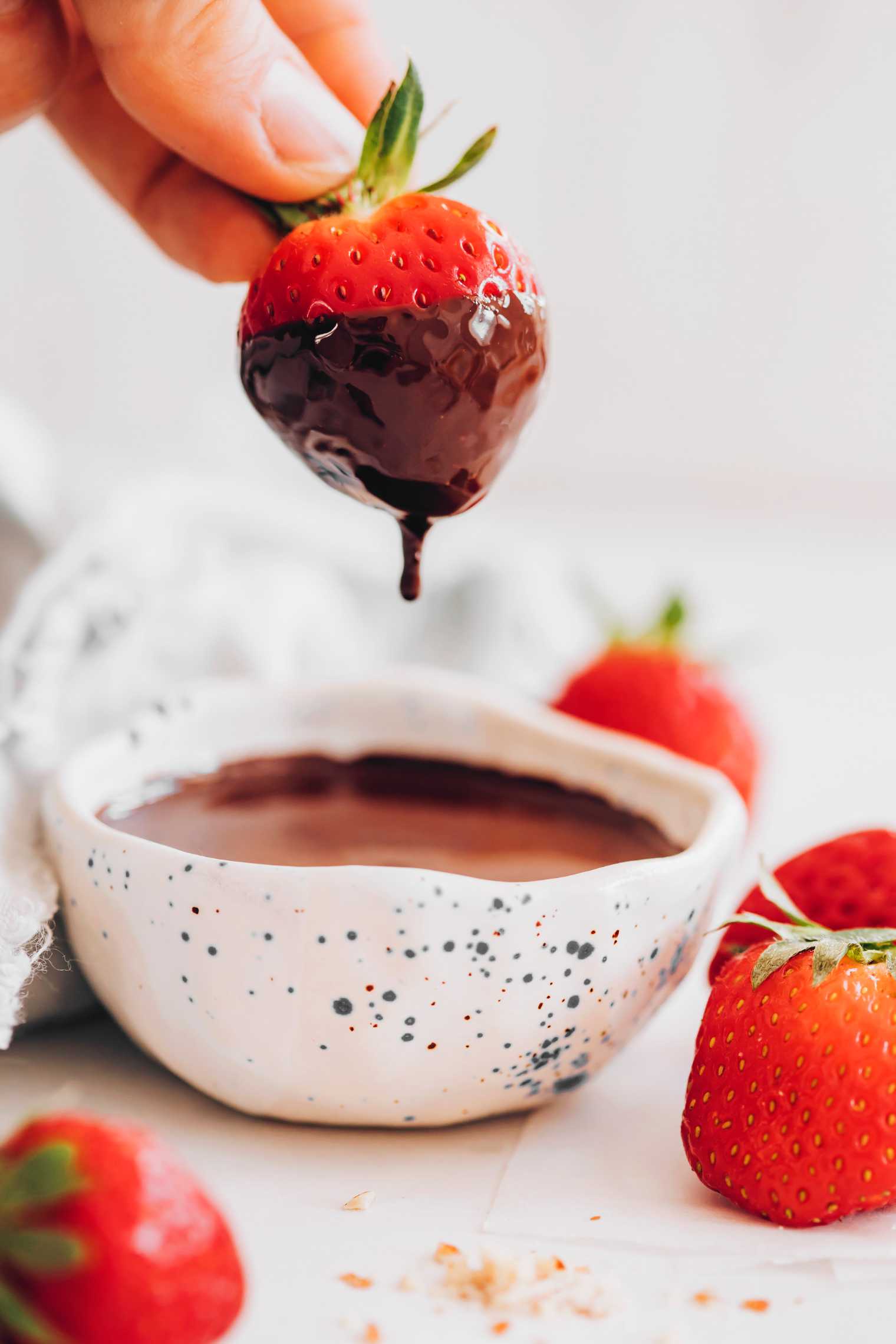 hand holding a fresh strawberry and dipping it into melted vegan chocolate