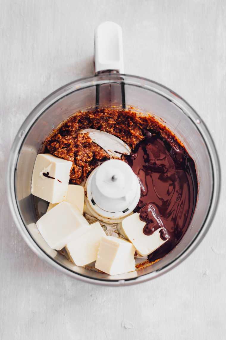 top view of a food processor that's fuilled with dates, melted chocolate and cubed silken tofu