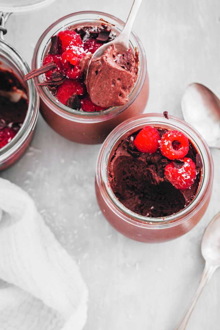 two glass jars with aquafaba chocolate mousse, coconut, raspberries and spoons