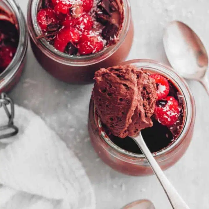 small glass jars with homemade vegan chocolate mousse topped with raspberries and coconut