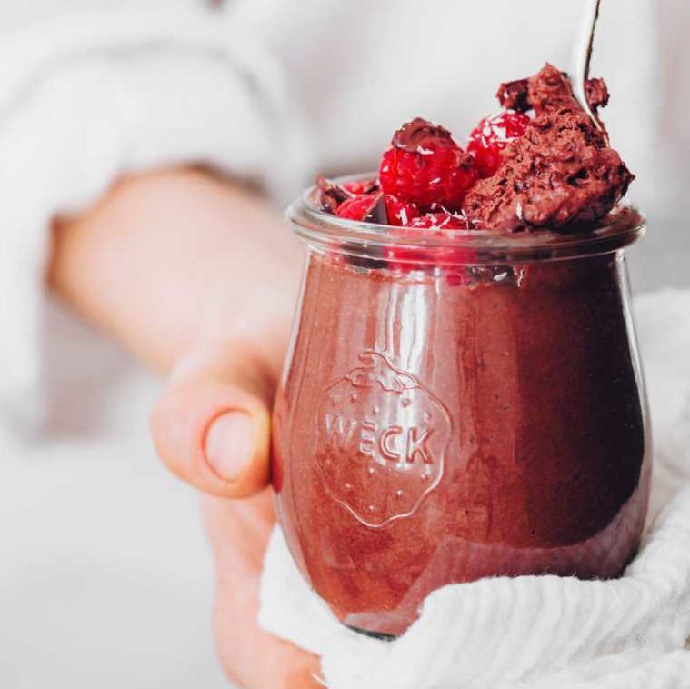 woman in white shirt holding a glass jar with homemade vegan protein chocolate mousse and a spoon
