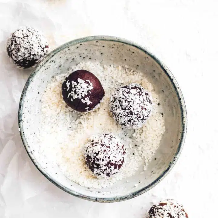 white table with a bowl filled with coconut shreds and homemade almond bliss balls