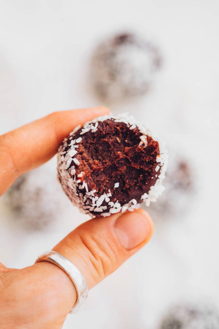 close up of a hand holding a vegan almond bliss ball with coconut coating between two fingers