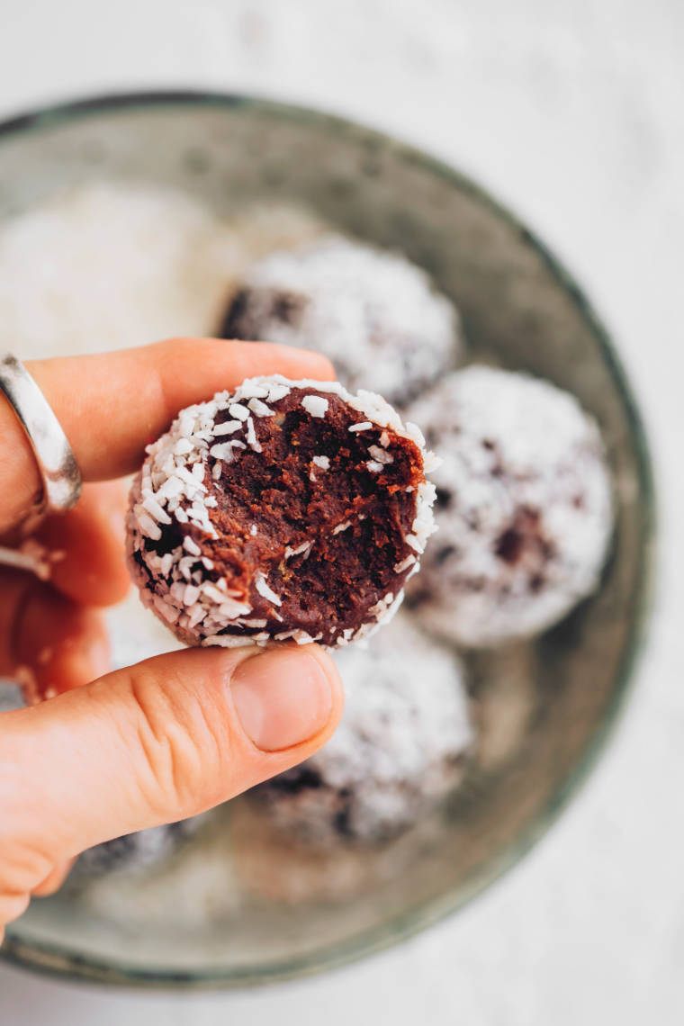 hand holding coconut almond energy ball over a bowl of more balls