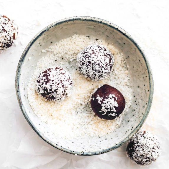 white parchment paper with several homemade vegan coconut almond bliss balls
