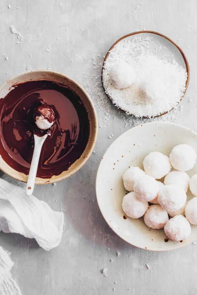 three bowls on a table containing melted chocolate, shredded coconut and raffaello bliss balls