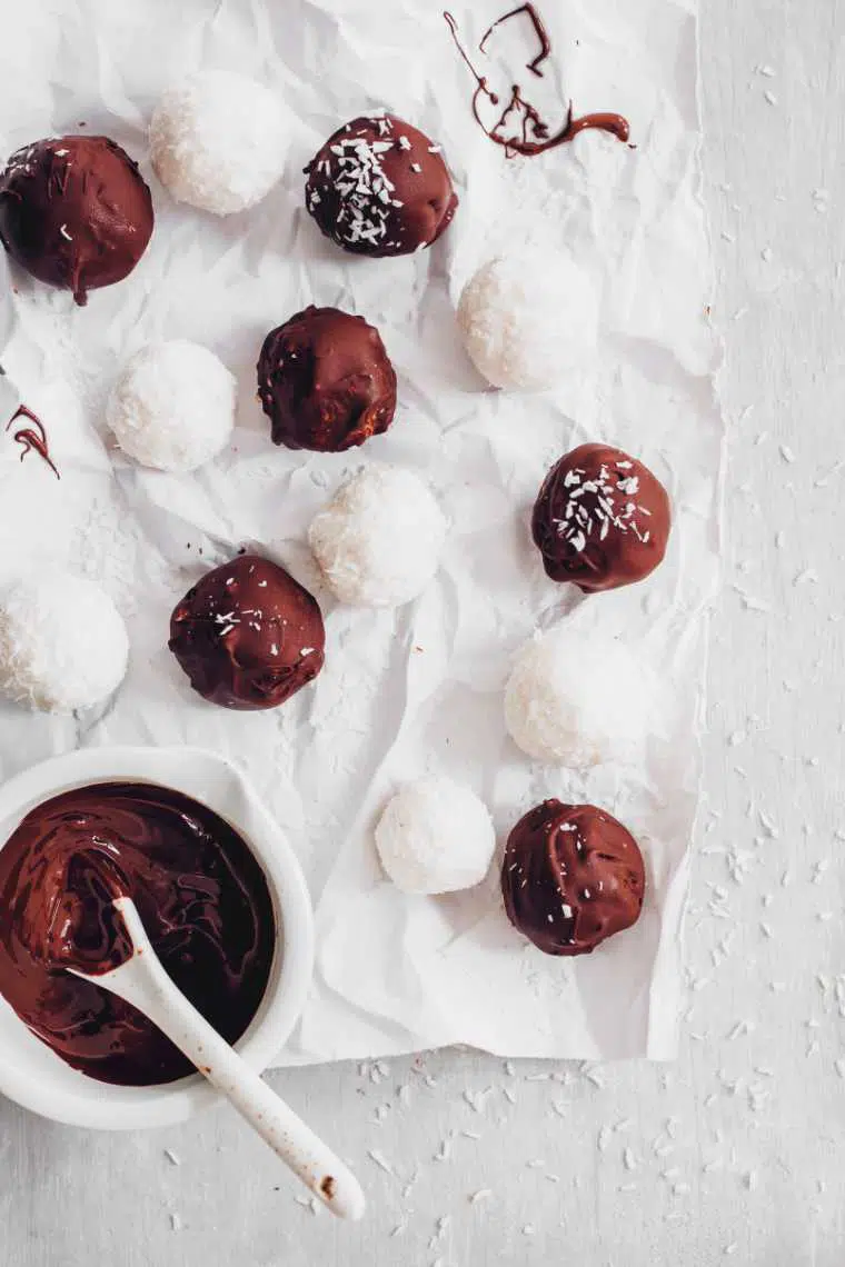white parchment paper on a table with a dozen homemade bounty and raffaello bliss balls