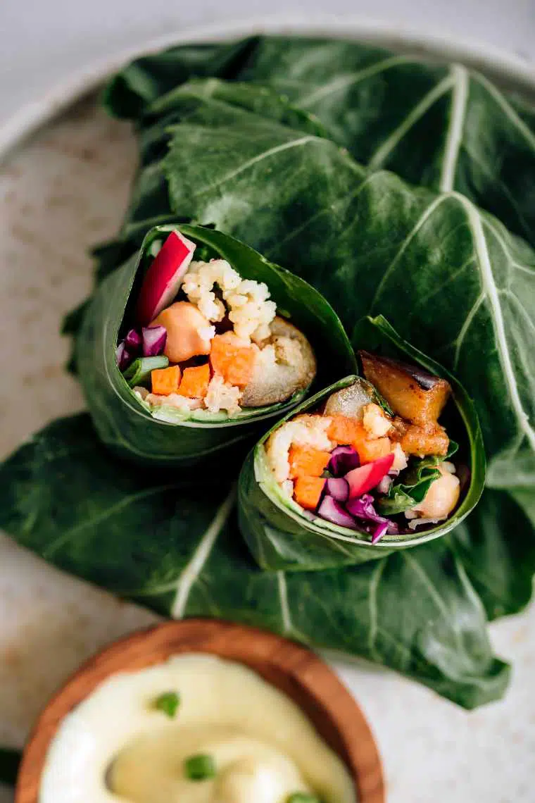white plate with a few rolled vegan collard wraps filled with millet next to a yogurt dip