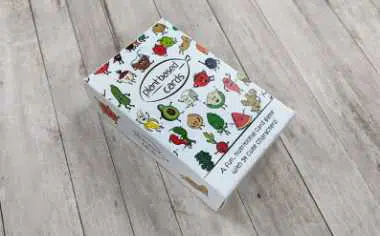 wooden floor with a white box on which lots of different fruits and vegetables are draw and plant-based cards for a game inside