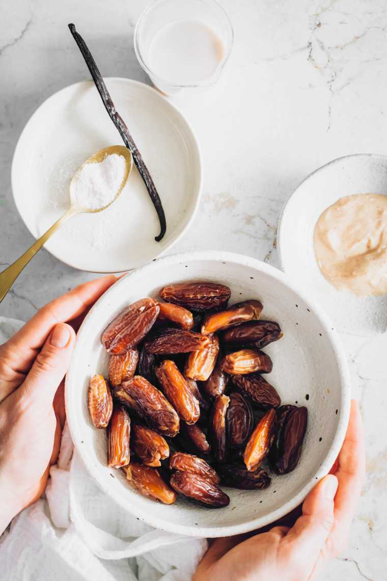 white table with different bowls containing dates, almond butter, salt and vanilla