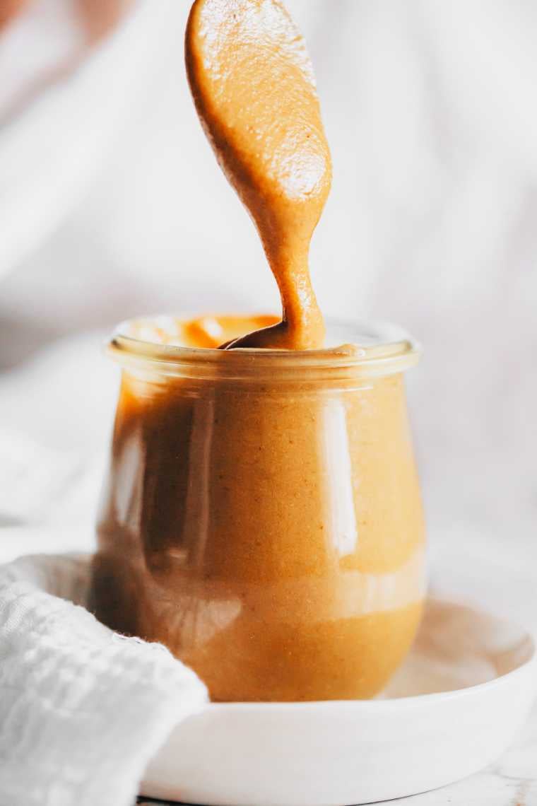 small white plate on a table with a glass jar of homemade vegan date caramel dripping from a spoon