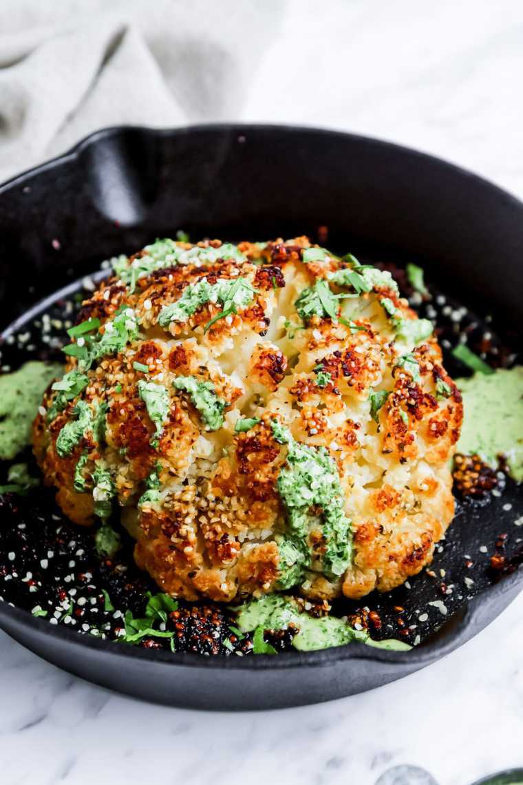 black pan with a whole roasted cauliflower head and green sauce