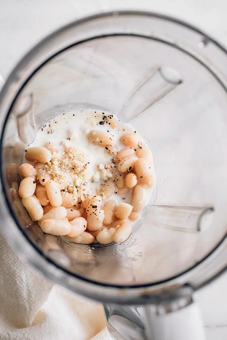 top view of open blender jar with white beans, soy milk and spices in it