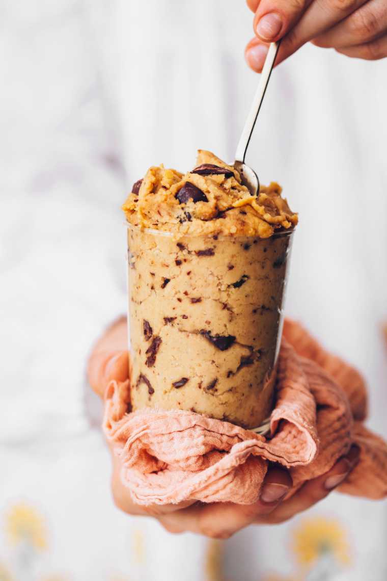 woman in white dress holding a glass with edible vegan cookie dough and a spoon