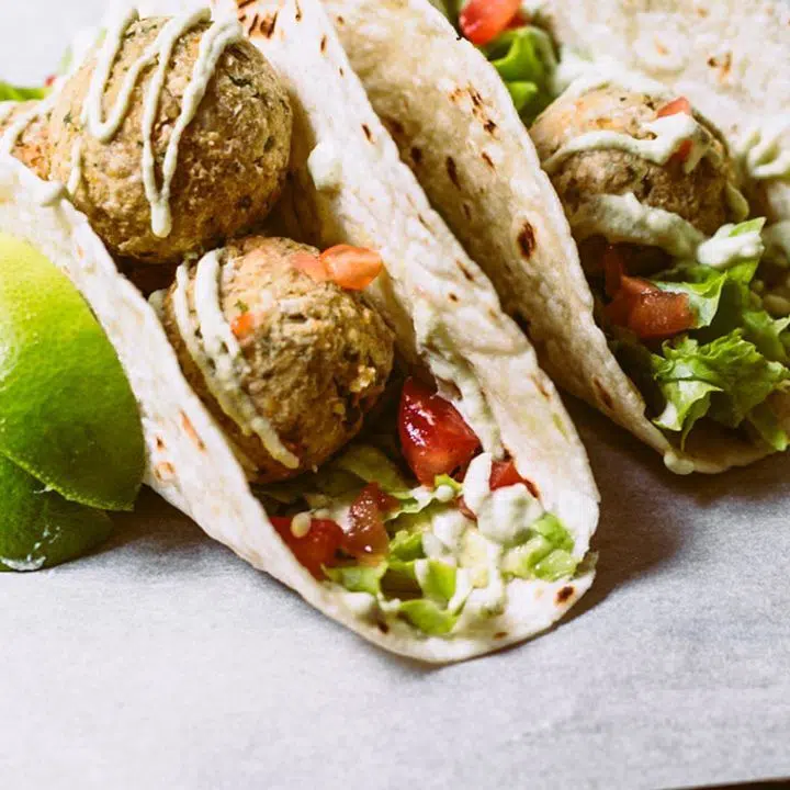 two taco shells that are filled with fresh veggies, baked falafel and drizzled with homemade vegan cashew sour cream