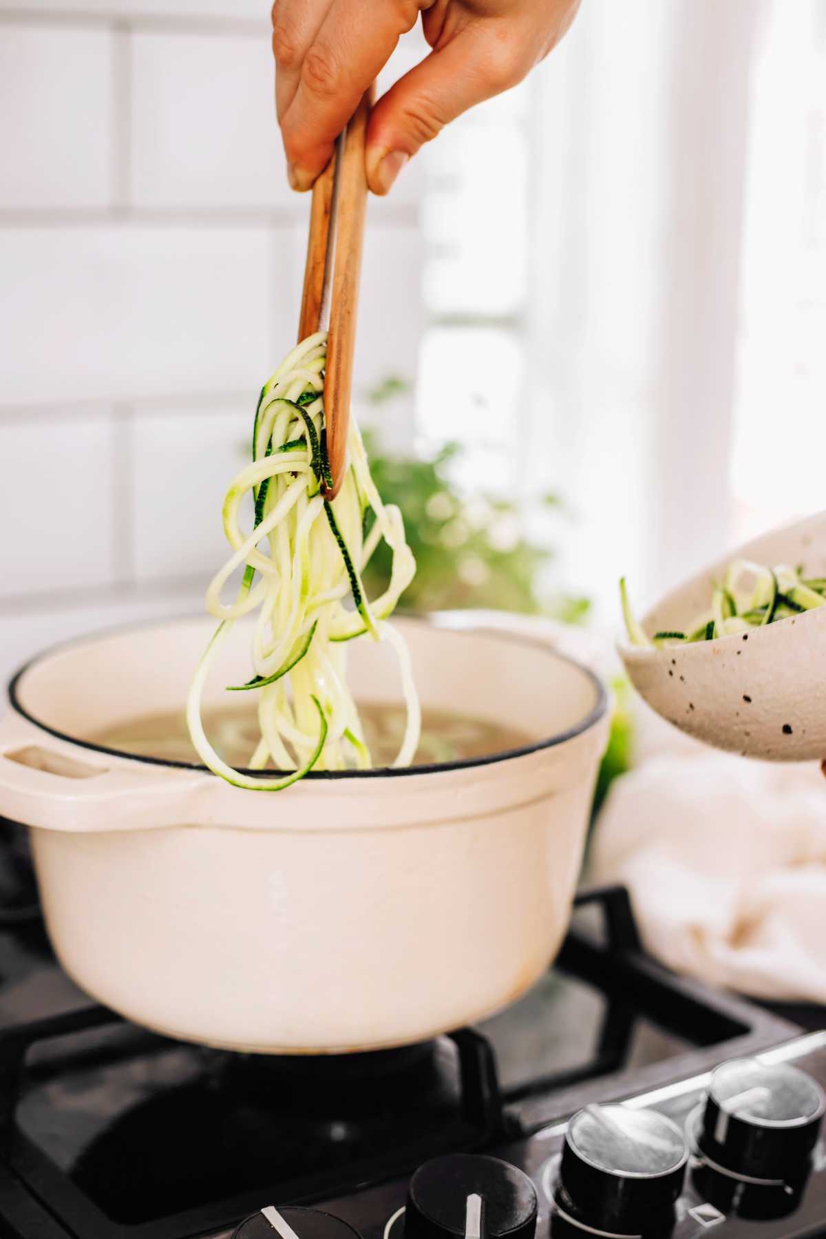 zoodles being added to a pot with waster and pasta