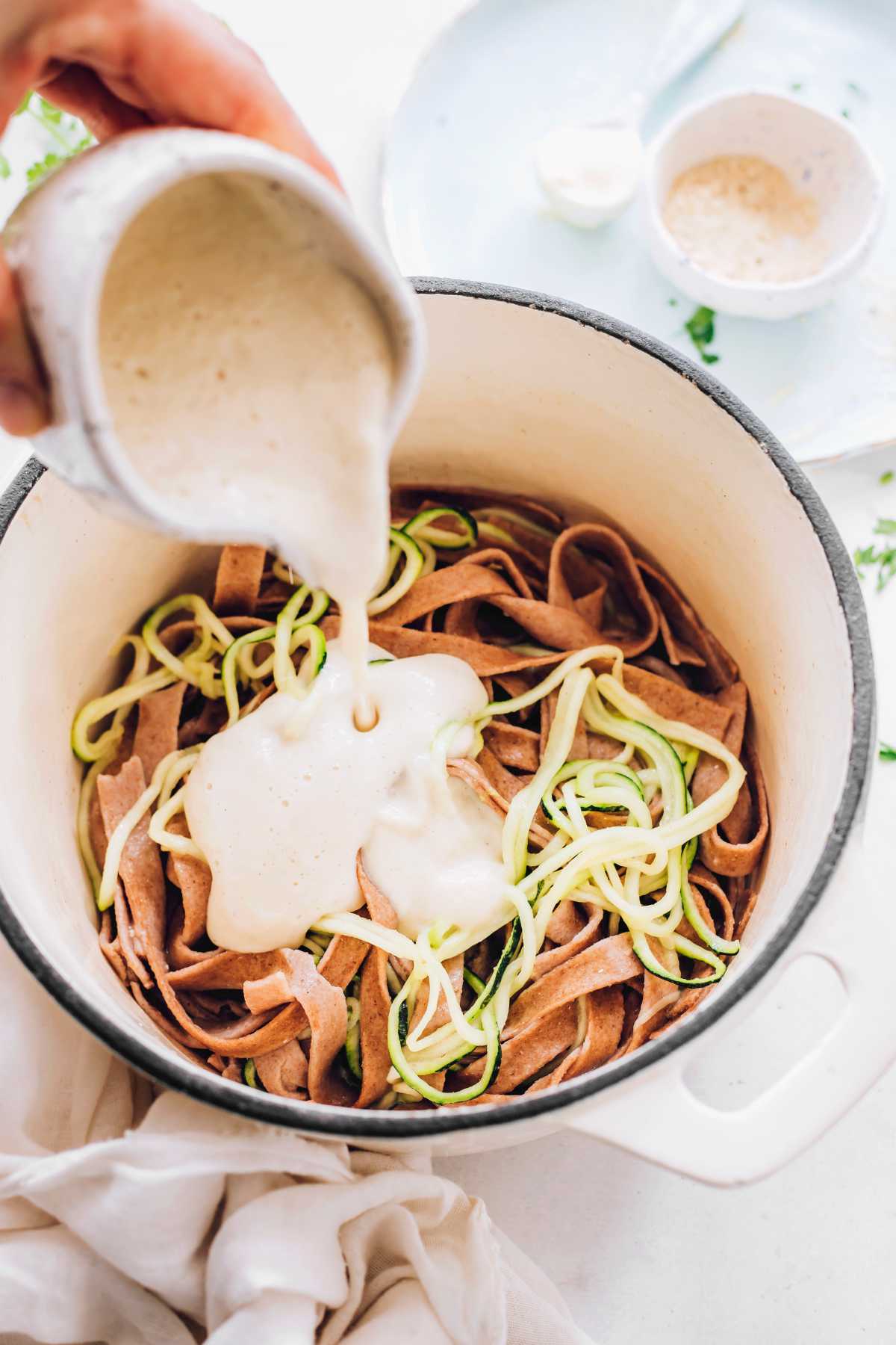 whole wheat pasta and zoodles being topped with Alfredo sauce