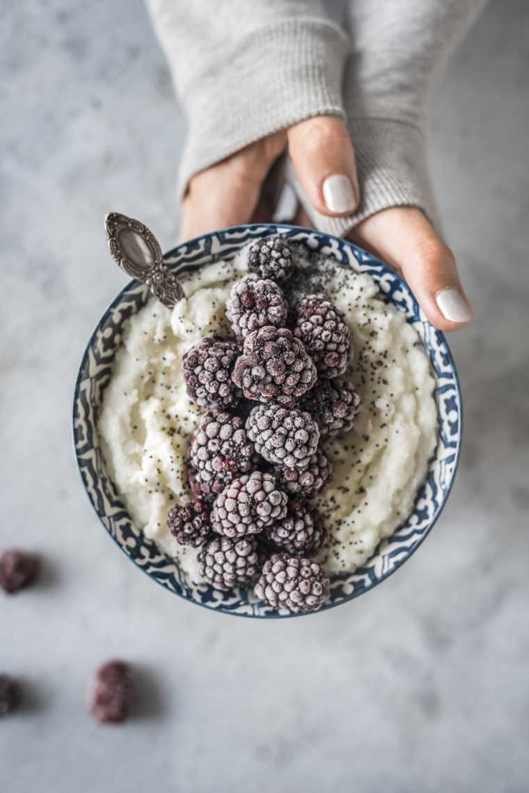 Woman holding bowl with frozen black berries on top of oatmeal