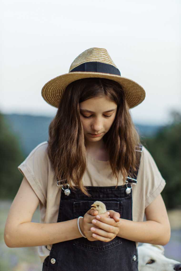 girl with a hat holding a little chick very carefully