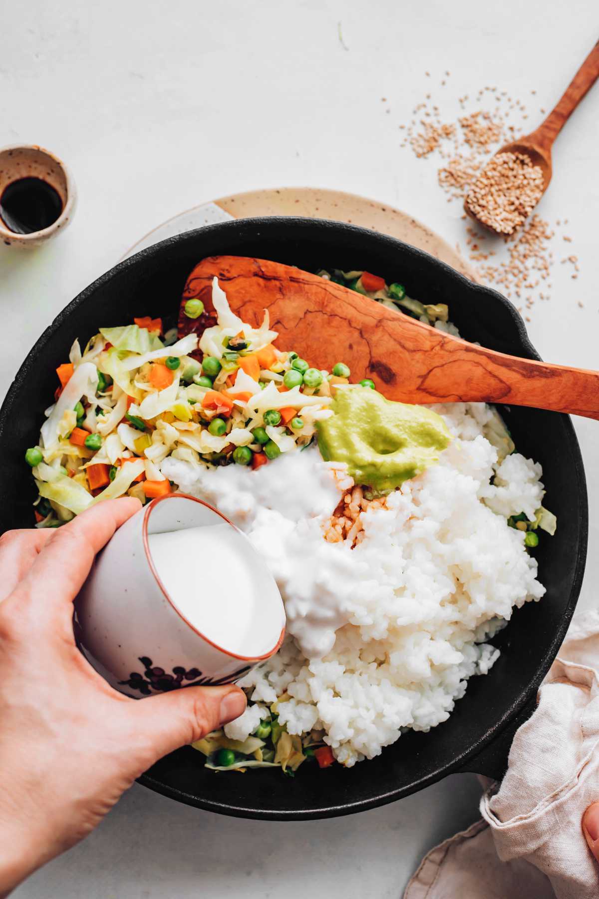 pouring coconut milk in pan over rice and veggies